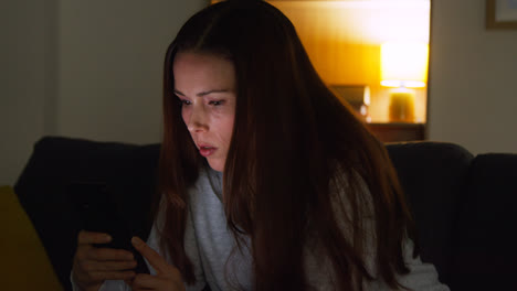 Anxious-Woman-Sitting-On-Sofa-At-Home-At-Night-Looking-At-Mobile-Phone-Concerned-About-Social-Media-Or-Bad-News-2